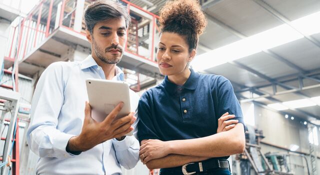 COLOUR-IMAGE_two-colleagues-looking-over-a-tablet-in-factory_apr26