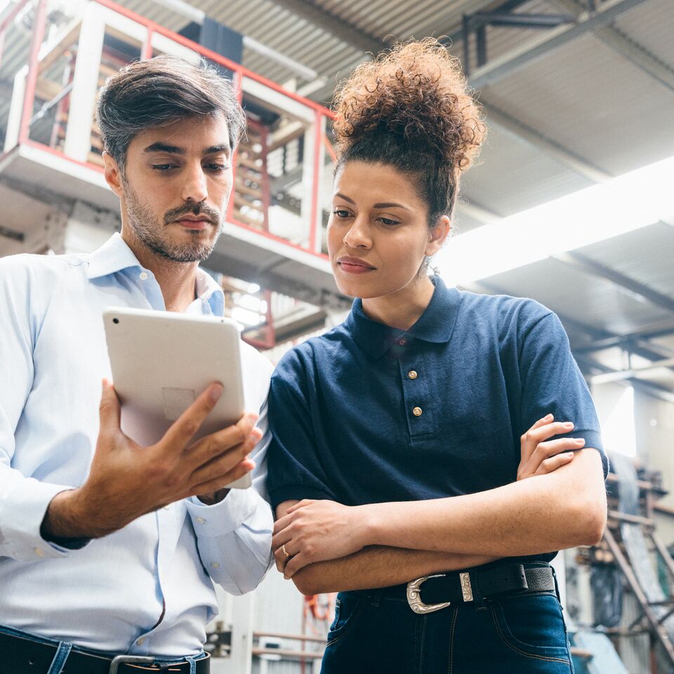 COLOUR-IMAGE_two-colleagues-looking-over-a-tablet-in-factory_apr26